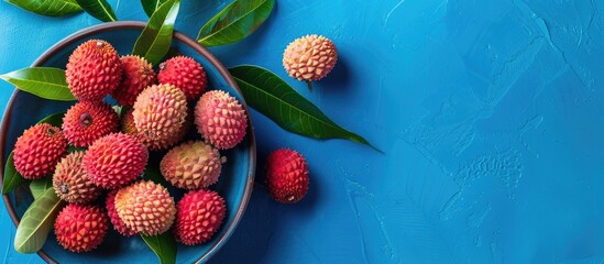 Fototapete - Flat lay of fresh ripe lychees with leaves on a blue backdrop offering copy space for text