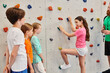 © LIGHTFIELD STUDIOS - A man teaches a diverse group of children how to climb a rock wall in a vibrant, energetic environment.