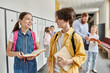 © LIGHTFIELD STUDIOS - A boy and girl, part of a diverse group of kids, stand next to each other in a hallway, awaiting instructions from their lively teacher.