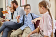 © LIGHTFIELD STUDIOS - A male teacher instructs a group of diverse kids in a bright, lively classroom setting, sitting close to each other and engrossed in learning.