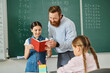 © LIGHTFIELD STUDIOS - A man teacher sharing a book with a young girl in a colorful classroom filled with students eagerly listening to the story.