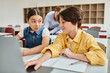 © LIGHTFIELD STUDIOS - A boy and a girl engage attentively at a table with a laptop, absorbed in a shared learning experience