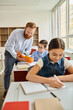 © LIGHTFIELD STUDIOS - A man standing at a desk, teaching a group of students in a vibrant classroom setting.