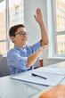 © LIGHTFIELD STUDIOS - A young boy sits at a desk in a bright, lively classroom, raising his hand to participate in the lesson.