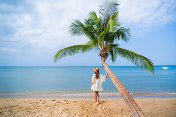 Alone woman traveler standing under a palm tree while relaxing on a tropical sandy island and enjoying idyllic and beautiful moment life