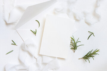 Wall Mural - Blank card and envelope near white silk ribbons and rosemary leaves top view, wedding mockup