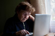 © De Visu - An elderly woman working on her laptop at home, teaching herself new skills.
