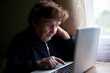 © De Visu - An elderly woman typing on a laptop keyboard, learning on her own at home.