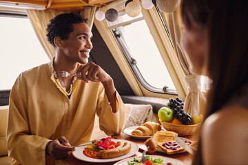 An interracial couple indulging in a delightful lunch inside a camper van, creating a romantic ambiance.