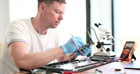 Canvas Print - Concentrated man fixes printed circuit board of broken laptop in workshop. Skilled master works in repair service center slow motion