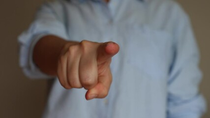 Wall Mural - Cropped shot of a young woman in a blue shirt pointing forward into the screen with her hand on a grey background. Pointing finger gesture. The sign that means I choose you. Changing focus