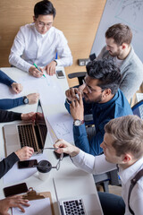 Wall Mural - Mixed race team of experienced marketers gather around a table to do research and implement new ideas. High angle view of multi-ethnic business people discussing in board room meeting