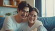© PAPAGAP - Happy couple in love smiling and embracing each other while sitting on a comfortable couch in a cozy home environment.