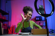 © amnaj - Young entrepreneur smiles and gives the ok sign while recording a video in her office and unpacking a box for her followers