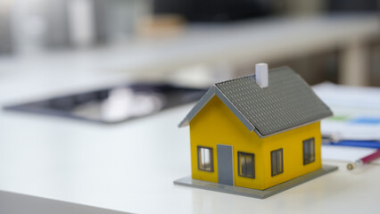 Yellow toy house standing on office desk with insurance, contract and mortgage documents in blurry background, real estate concept