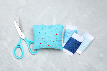 Poster - Light blue pincushion with sewing pins, scissors and threads on grey table, flat lay