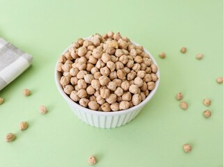 Raw dry chickpea in small ceramic bowl on green background. Traditional ingredient for cooking hummus. Middle Eastern and Mediterranean cuisine. Selected focused