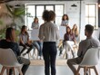 © Ace64 Studio - Confident female business coach teaches small group of people new business knowledge. People are sitting on chairs in office of business center listening to woman standing with her back to camera