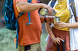 © Mediteraneo - Married couple having coffee break from hiking. They are pouring coffee from a thermos and they are also carrying backpacks and hiking poles.