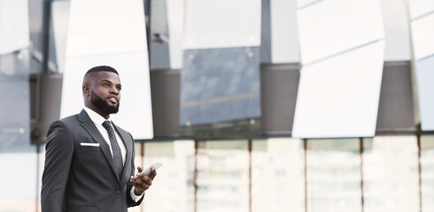 Keep Busy. Thoughtful African American Businessman Holding Cellphone And Laptop Standing In Urban Area. Copy Space