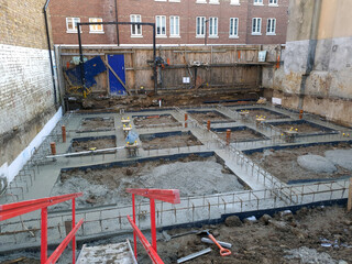 Construction site with workers building a house extension, installing foundations, steel reinforcement, and concrete footings. Urban construction process for residential development. 