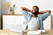 © Prostock-studio - Life is good. Cheerful african american employee sitting on chair with hands behind his head, relaxing at workplace in office.