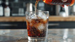 © Rabil - A hand pours soda into a glass with ice cubes.