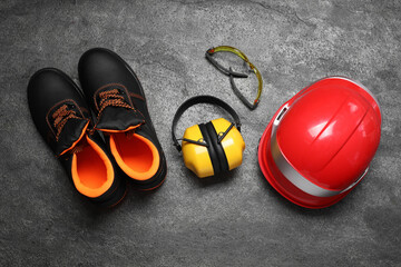 Wall Mural - Pair of working boots, hard hat, protective goggles and earmuffs on grey surface, top view