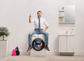 Wall Mural - Businessman sitting on top of a washing machine and gesturing thumbs up