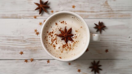 Chai latte in a white cup topped with star anise and sprinkled with cinnamon, viewed from above on a light wooden table, warm and cozy atmosphere