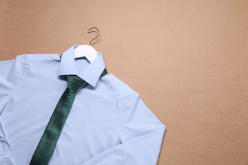 Wall Mural - Hanger with shirt and necktie on beige background, top view. Space for text