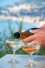 Wall Mural - Pouring of sparkling wine, cava or champagne in two coupe glasses on table with view on blue sea, Menton and Monte-Carlo, French Riviera, France is summer