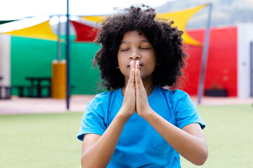 Wall Mural - Tranquil biracial schoolgirl practicing yoga meditation in school playground, with copy space