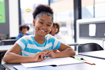 Sticker - Portrait of happy african american schoolgirl sitting at desk in school classroom