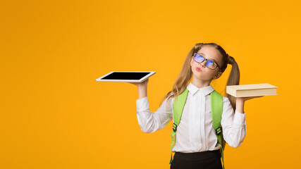 Wall Mural - Books Or Gadgets. Nurdy School Girl Comparing Schoolbook And Digital Tablet Over Yellow Background. Empty Space