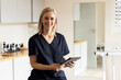 © Wavebreak Media - Holding tablet, woman in medical clinic smiling and wearing scrubs