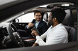 © sofiko14 - Discussing car features, options, and purchase details with friendly conversation. Caucasian car dealer sit inside vehicle with African American buyer.