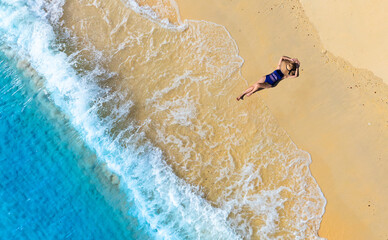 Wall Mural - Aerial view of beautiful young woman in black swimsuit lying on sandy beach near blue sea with waves at sunset Summer vacation at Andaman Island	