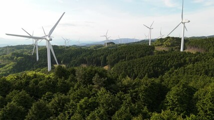 a cluster of wind turbines for generating electric power in a valley surrounded by green forest. win