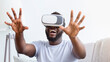 © Prostock-studio - African American man wearing a VR headset is seated on a couch, both hands outstretched, as he laughs in delight at something in the virtual world.