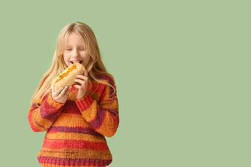 Wall Mural - Cute little girl eating tasty hot dog on green background