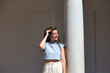 © @skuder_photographer - young and beautiful latin woman is leaning on a white marble column and touching her hair with her hands. The woman is happy and smiling on the sunny day in the city of Seville, Spain.