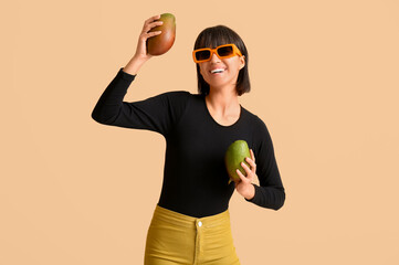 Poster - Beautiful young woman with ripe mangoes on beige background