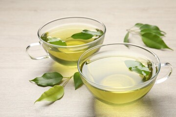 Poster - Refreshing green tea in cups and leaves on wooden table, closeup