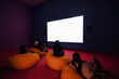 © Kajornsiri - White cinema screen mockup with silhouettes of spectators setting on beanbags in colorful room