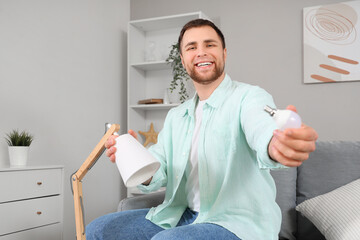 Wall Mural - Young man changing light bulb in desk lamp in living room