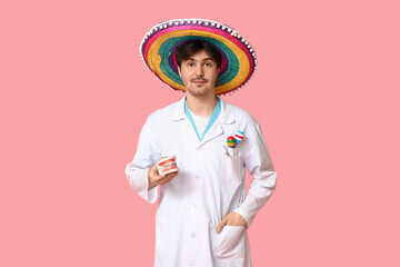 Wall Mural - Young male dentist with sombrero, maracas and jaw model on pink background