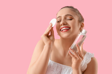 Wall Mural - Young woman with micellar water and cotton pad on pink background, closeup