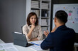 © Wasana - A woman and a man are sitting at a desk with a white board behind them