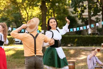 Canvas Print - Young couple in traditional German clothes dancing outdoors. Octoberfest celebration